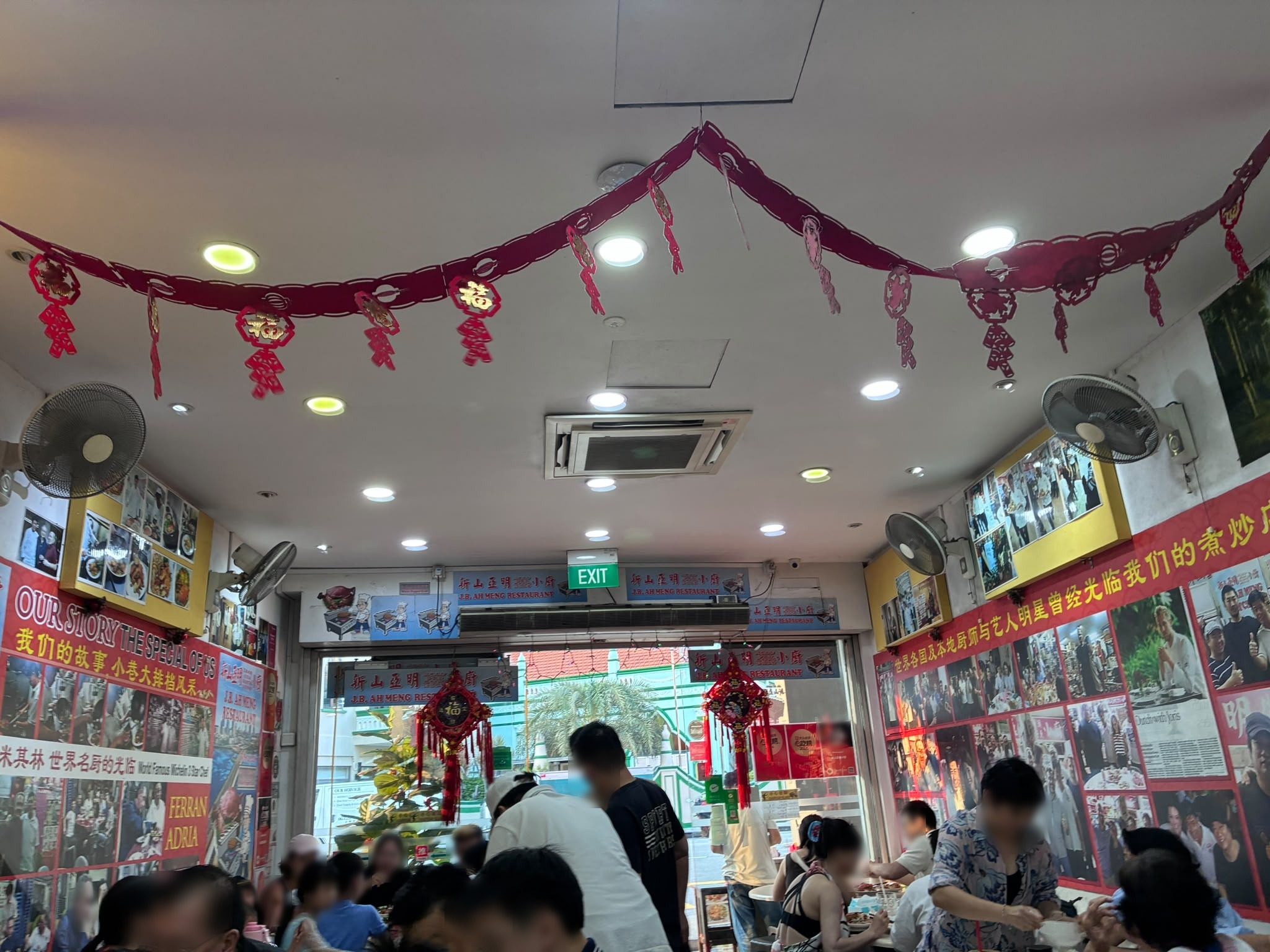 Interior of J.B. Ah Meng Restaurant with walls covered in press clippings (faces blurred)
