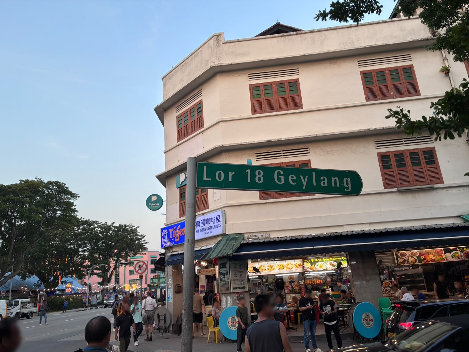 Street sign for Lorong 18 Geylang above a coffee shop in Singapore (faces blurred)