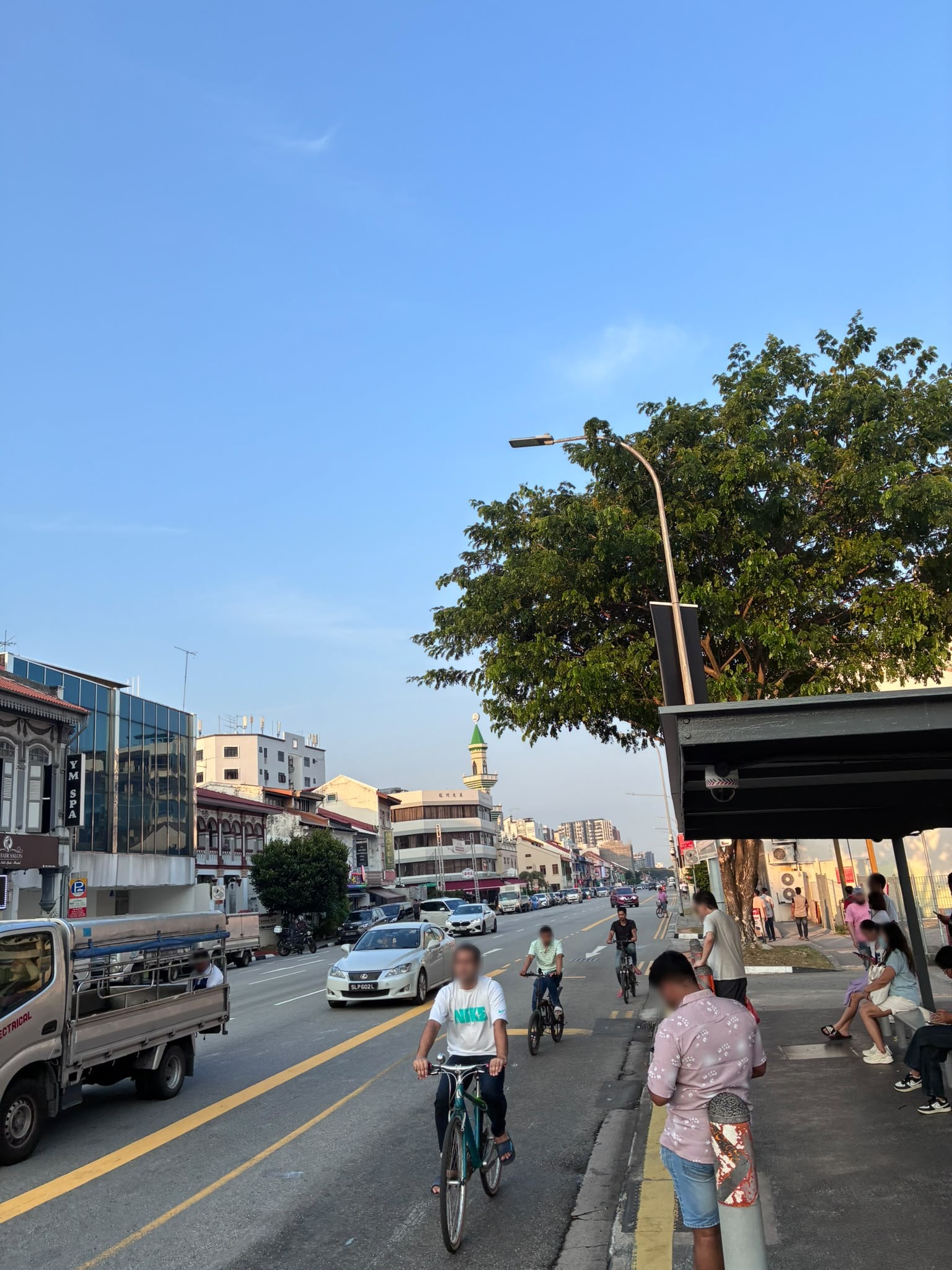 Cyclists on Geylang Road with a mosque minaret in the background (faces blurred)