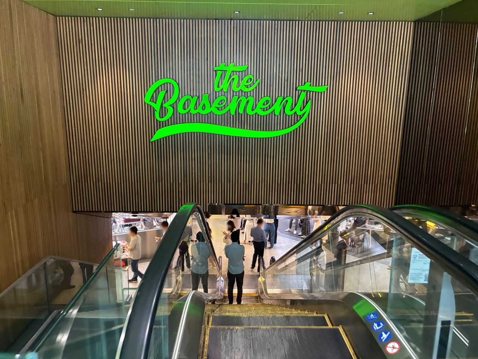 Escalator down to The Basement food hall with green neon sign, Hong Leong Building Singapore (faces blurred)