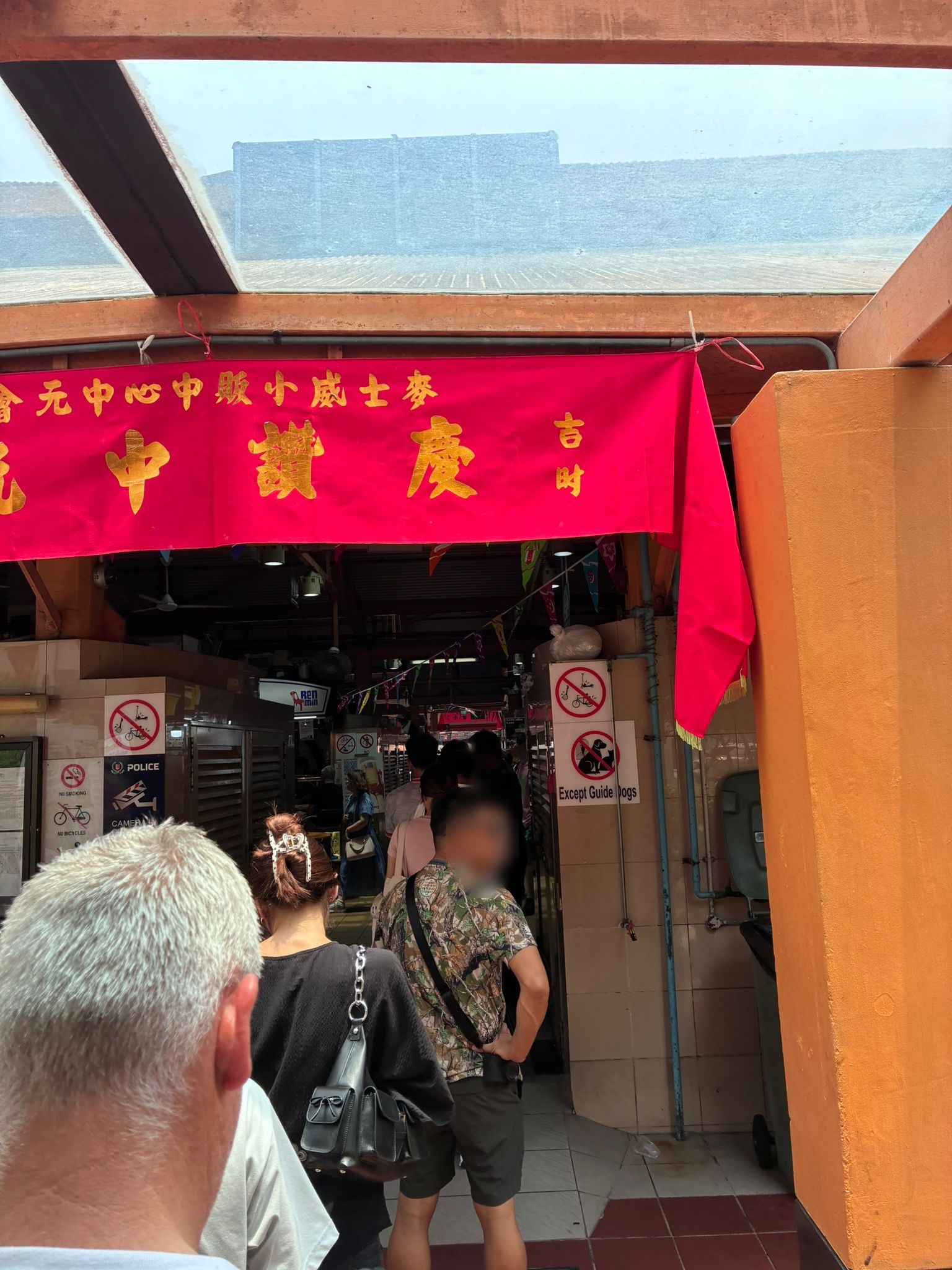 Entrance of Maxwell Food Centre under a red Hungry Ghost Festival banner (faces blurred)