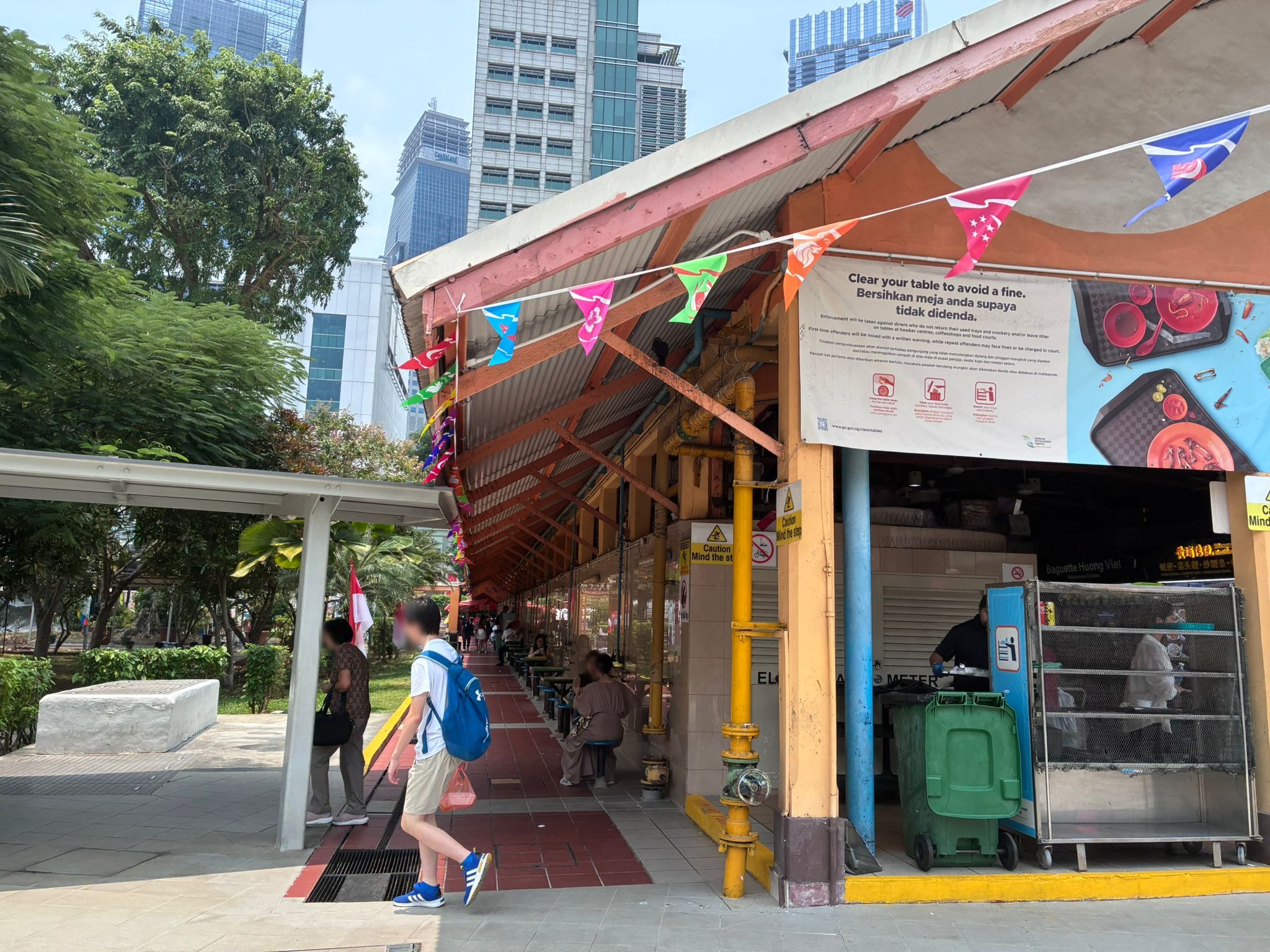 Side walkway of Maxwell Food Centre with a Clear your table to avoid a fine banner (faces blurred)