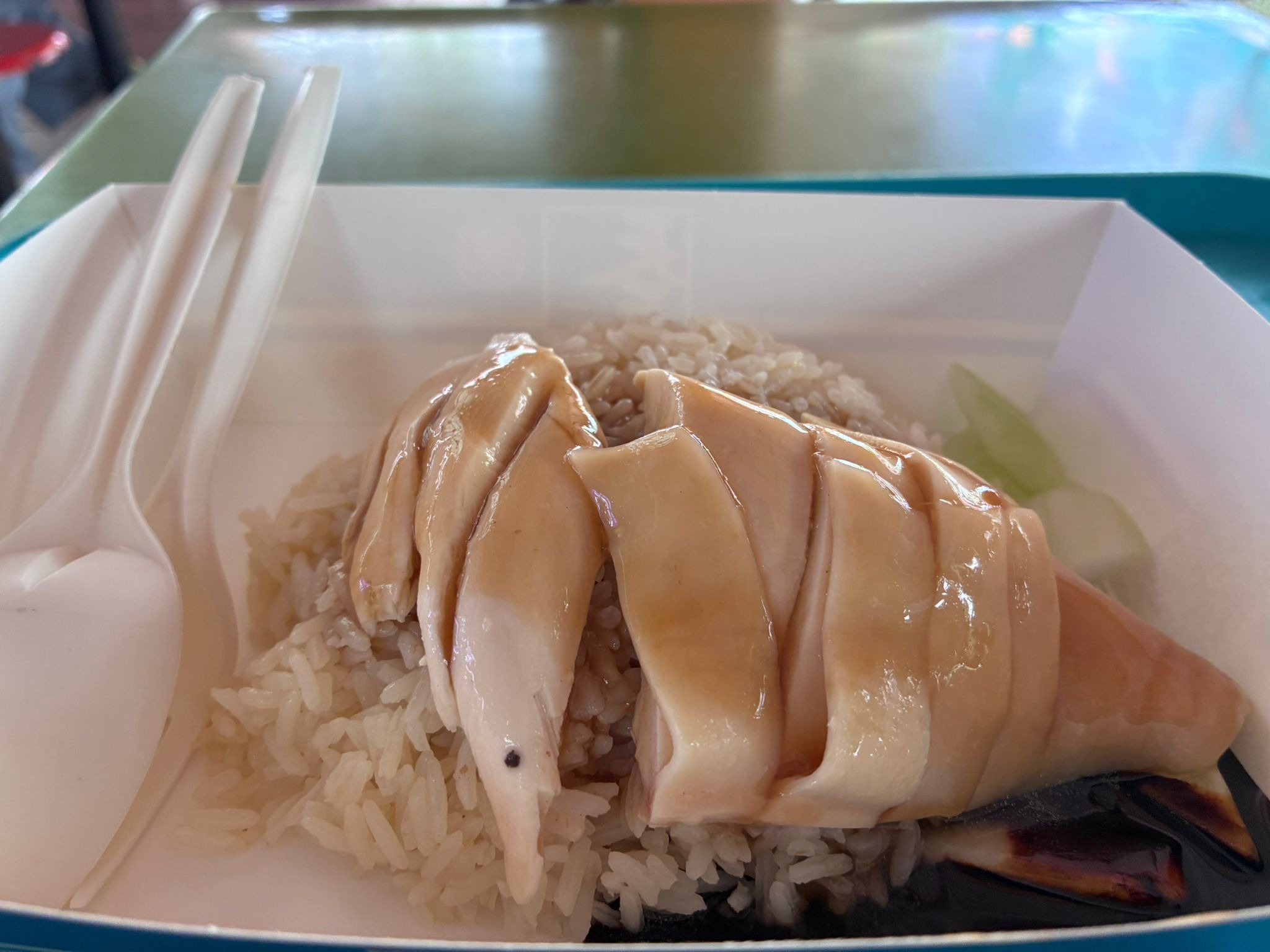 Close-up of steamed chicken slices with dark sauce over chicken rice