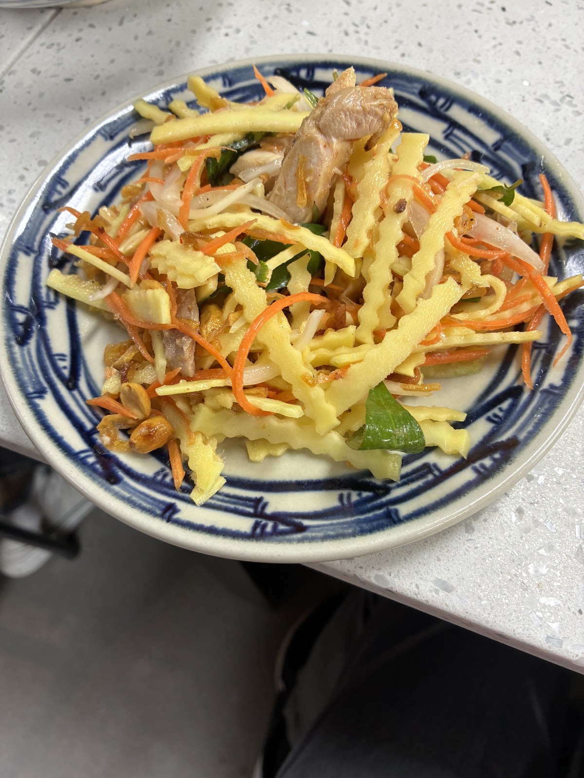 Green papaya salad with carrot, herbs and peanuts on a blue rimmed plate, Vietnamese cooking class