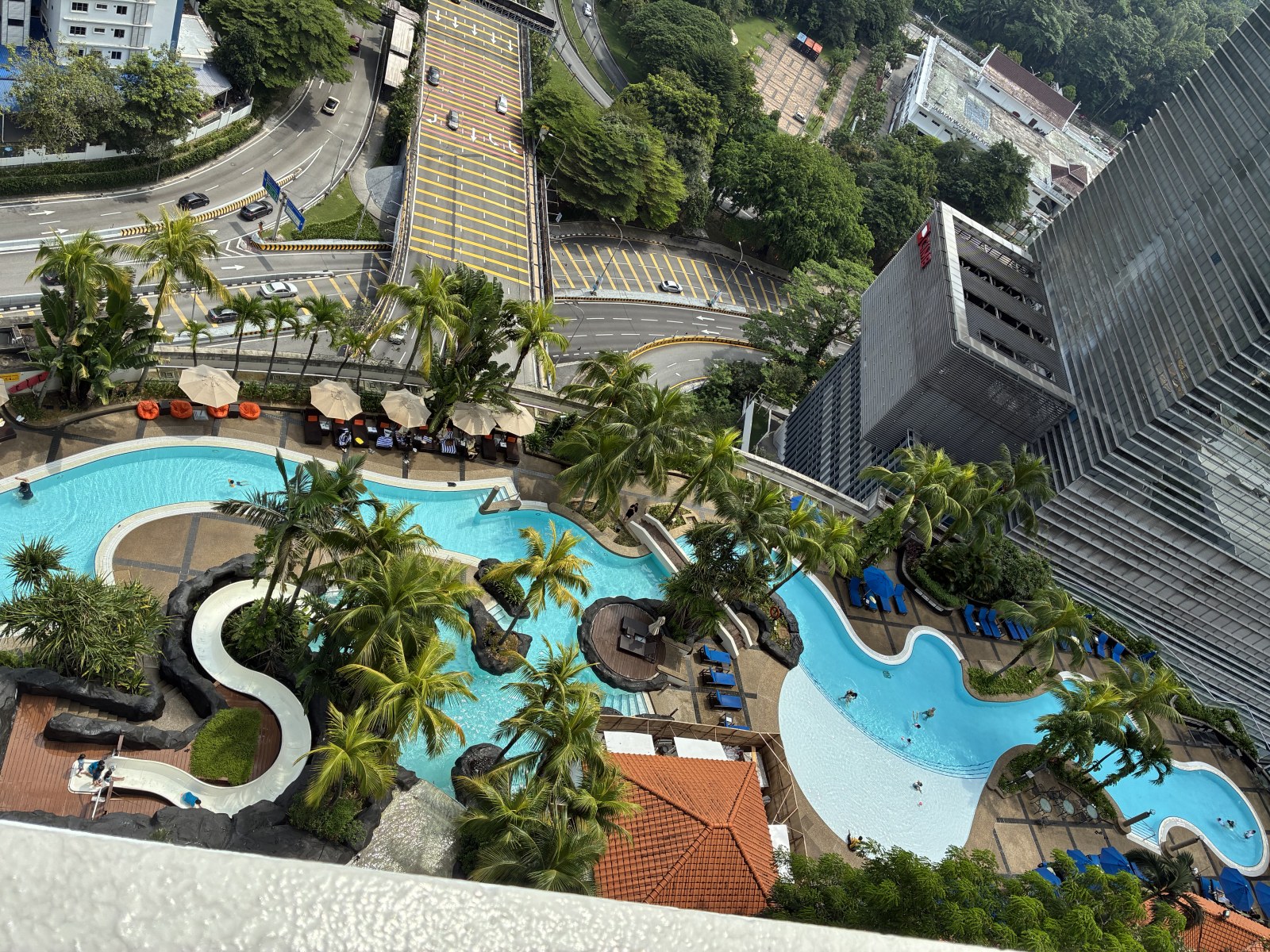 Large curved outdoor swimming pool with palm trees seen from a high floor at Hilton Kuala Lumpur, Malaysia