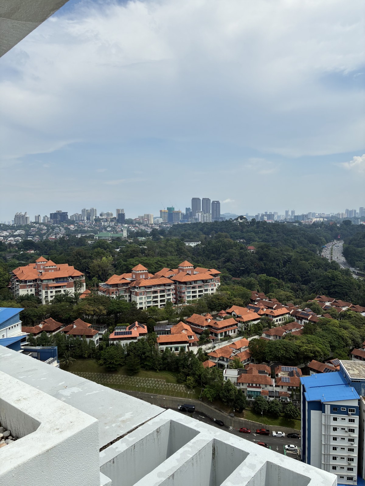 Red-roofed low-rise housing surrounded by trees seen from a high floor in Kuala Lumpur, Malaysia
