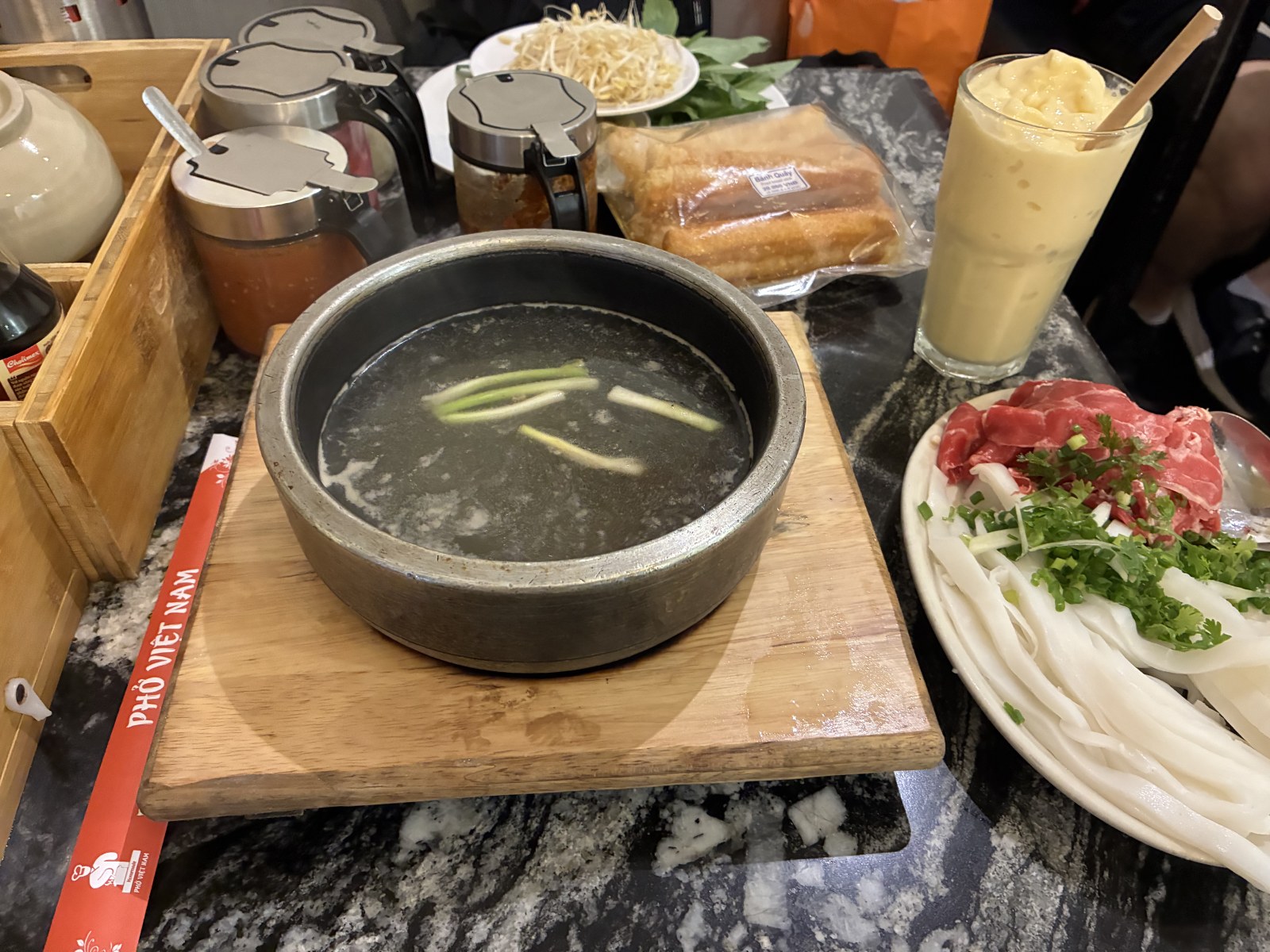 Pho served in a sizzling hot stone bowl with raw beef and noodles on the side, Ho Chi Minh City, Vietnam