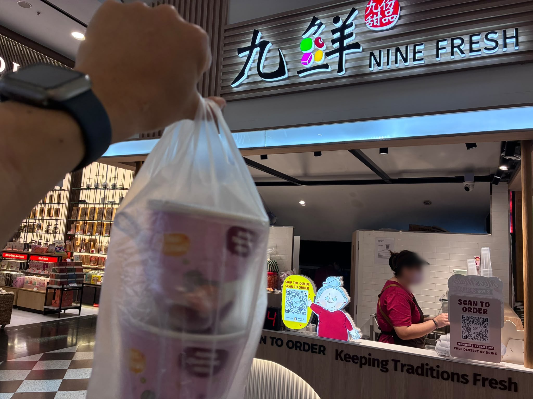 Takeaway bag of desserts in front of the Nine Fresh taro ball dessert counter in Singapore (faces blurred)